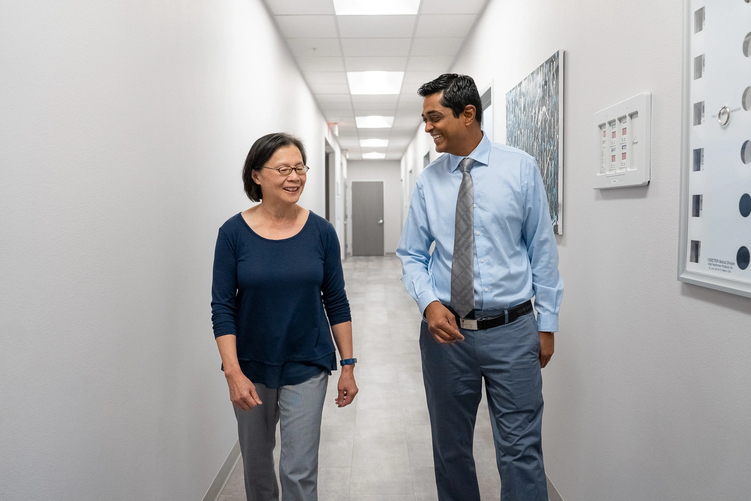Dr. Ajay Ganti, a dual-degree oral and maxillofacial surgeon, walks down a hallway with a patient, smiling and talking during a visit.